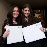 Two students hold their degrees and smile for a photo